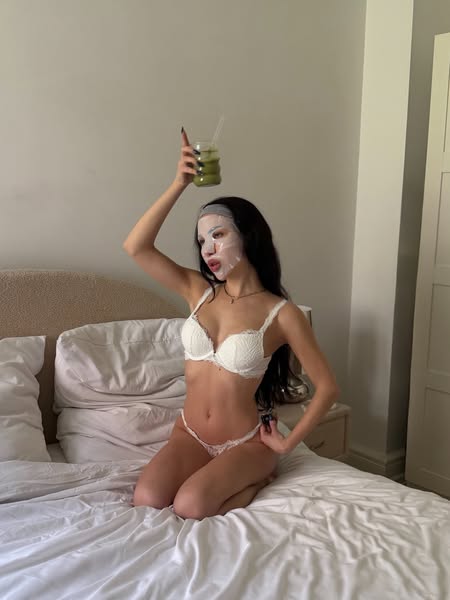 A woman wearing a face mask sits on her bed wearing lingerie and drinking matcha to showcase the product.
