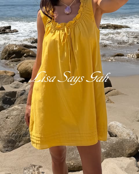 A product photo featuring a model wearing a yellow mini dress on a beach.