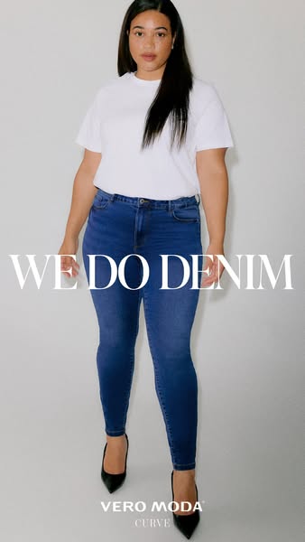 A woman models Vero Moda Curve jeans and a white t-shirt in front of a white background.