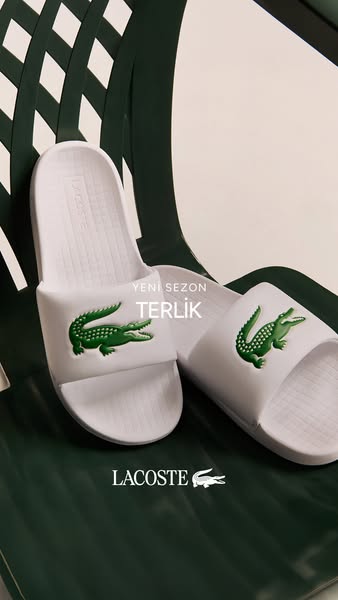 A product display for Lacoste featuring a pair of white slides with a green logo against a green and white background.