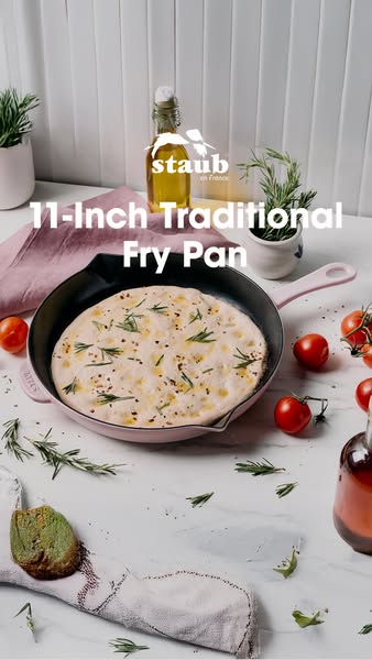This ad highlights a pink Staub 11-Inch Traditional Fry Pan. The product is shown with focaccia bread inside it, surroun