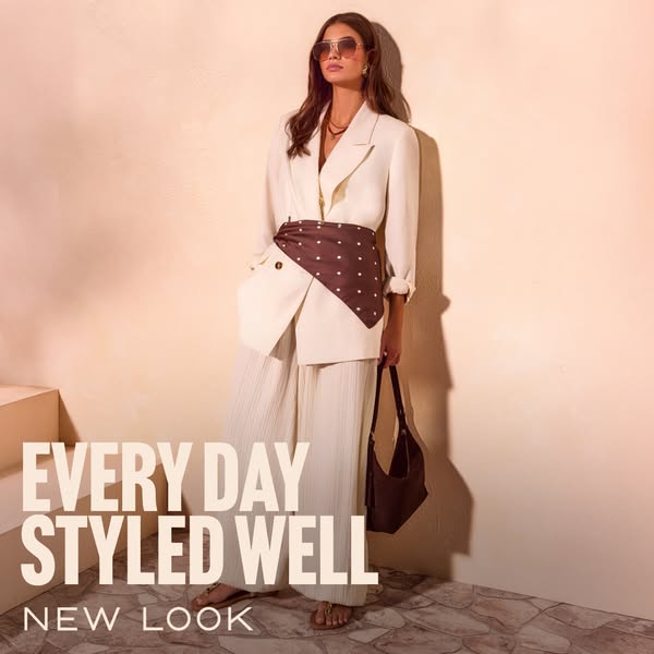 This ad showcases a woman wearing a white blazer and pants set, styled with a brown and white polka dot scarf, a brown p