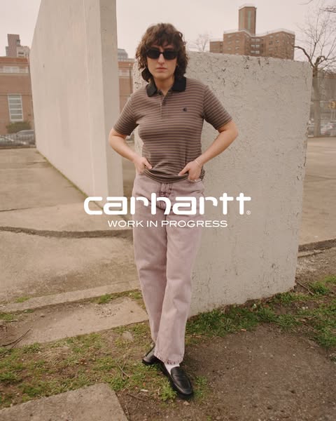 This ad features an image of a woman standing in front of a textured wall while wearing a Carhartt polo shirt and light 