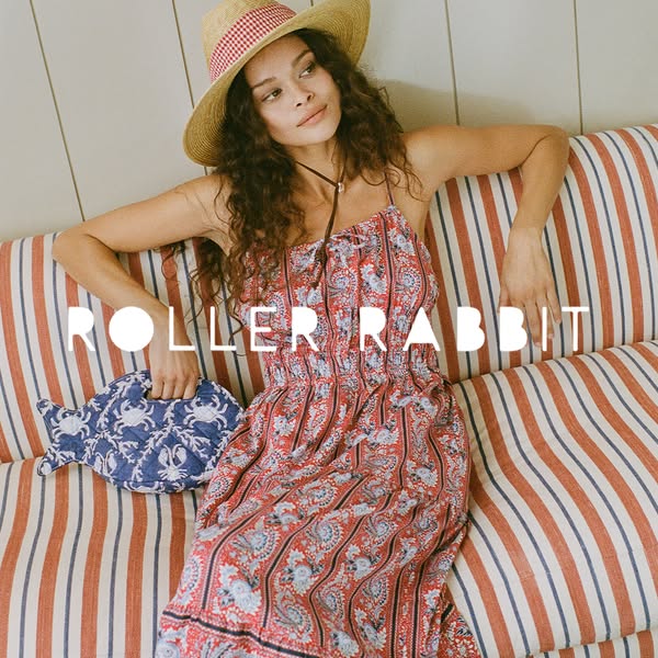 An image ad featuring a woman wearing a Roller Rabbit dress, hat, and holding a fish-shaped bag on a vertically striped 