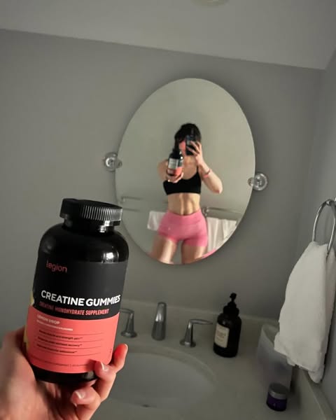 This ad features a woman in a bathroom holding a bottle of Legion brand creatine gummies. She is also visible in the mir