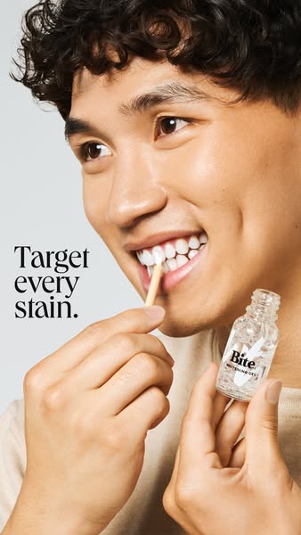 A close-up studio shot of a man demonstrating how to apply the Bite teeth whitening gel with a wooden applicator.