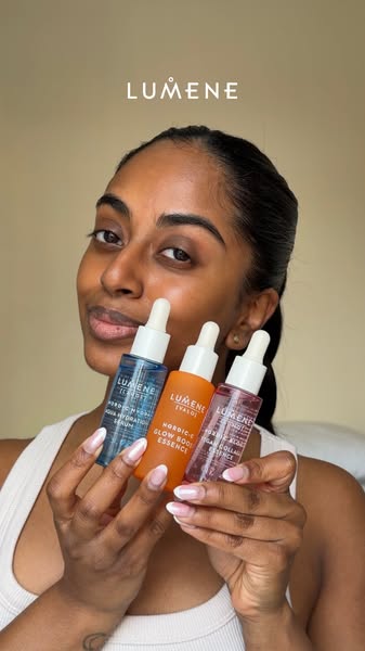 A woman is holding three different Lumene product bottles, all with a dropper applicator. Each of the bottles has a diff