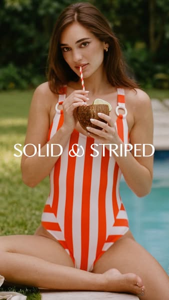 A woman in a red and white striped swimsuit is shown sitting and relaxing outside while drinking from a coconut.