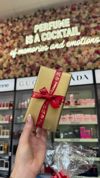 An image ad showcasing a gift-wrapped perfume in a store with a flower wall and various perfume brands in the background