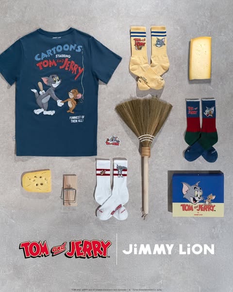 Flatlay image showing a Tom and Jerry branded t-shirt, socks, cheese, mousetrap, broom, product box, and sticker set aga