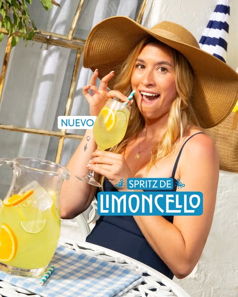 A woman in a sunhat drinks a lemon cocktail and an additional pitcher of the cocktail sits on the table, with a badge th