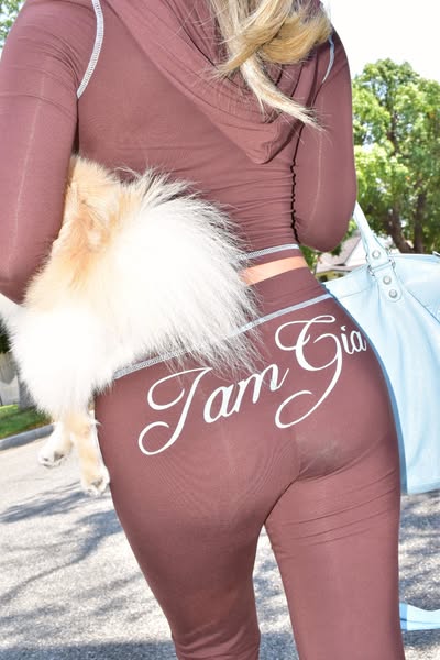 This image ad features a woman wearing a brown tracksuit with the brand name on the back. She is holding a dog and carry