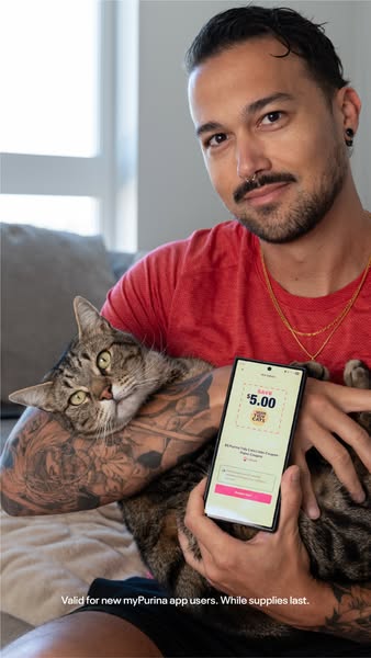 The ad features a man holding a cat and a phone. The phone displays a coupon for Purina cat food. The ad is likely targe