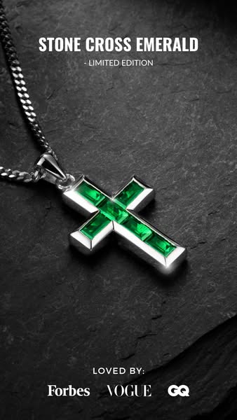 This ad features a close-up shot of a silver cross pendant with emerald stones on a silver chain, presented against a da