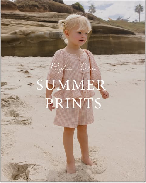 This ad showcases a young girl on a beach wearing a matching pink gingham top and shorts set by Rylee + Cru. The ad high