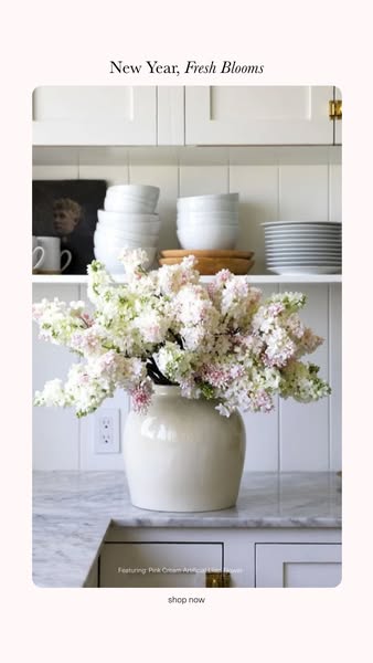 This image ad features a vase of pink and white artificial flowers on a marble countertop in front of white cabinets. Th