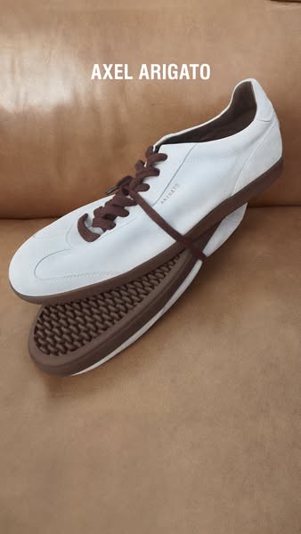 This ad features a photograph of an Axel Arigato shoe. The shoe is a white sneaker with brown laces and sole. The ad sim