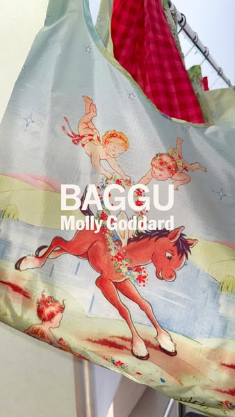 This ad showcases a Baggu brand reusable bag in a light blue color with a vintage-style illustration of cherubs and a ho