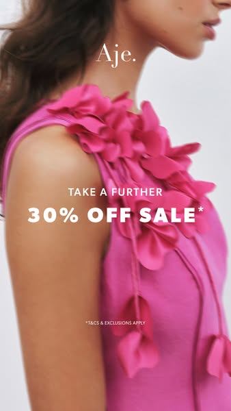 This image ad for Aje. features a close-up shot of a woman wearing a pink dress with floral embellishments. The ad promo