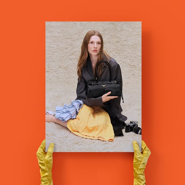 The ad showcases a black Prada handbag, held in front of a woman sitting on a textured rug. The handbag is the focal poi