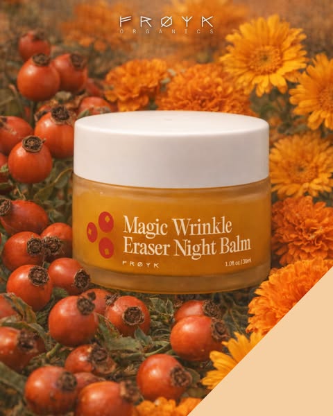 A close-up of Frøyk Organics' Magic Wrinkle Eraser Night Balm surrounded by rosehips and marigolds is shown in an ou