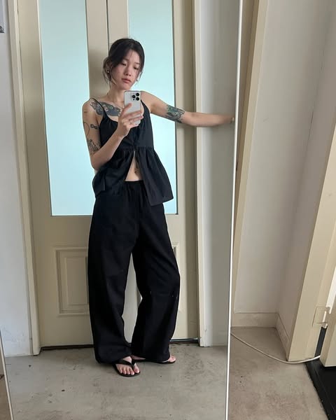 A woman takes a mirror selfie wearing a black top and pants.