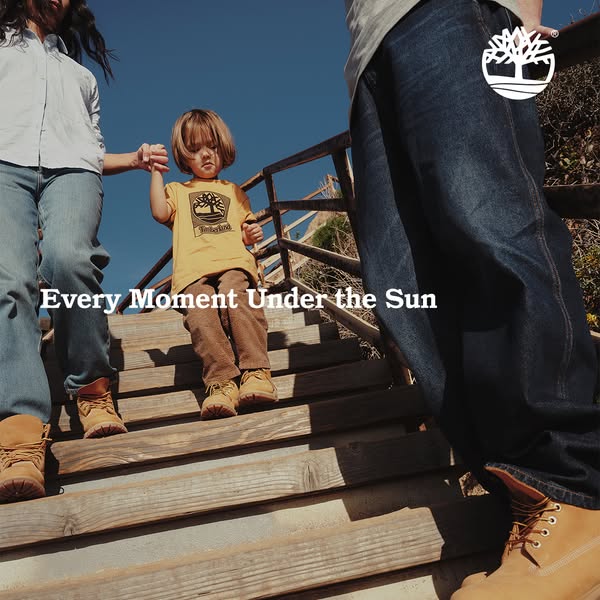 An ad featuring Timberland boots being worn by a family descending a set of wooden stairs outside, under a bright blue s