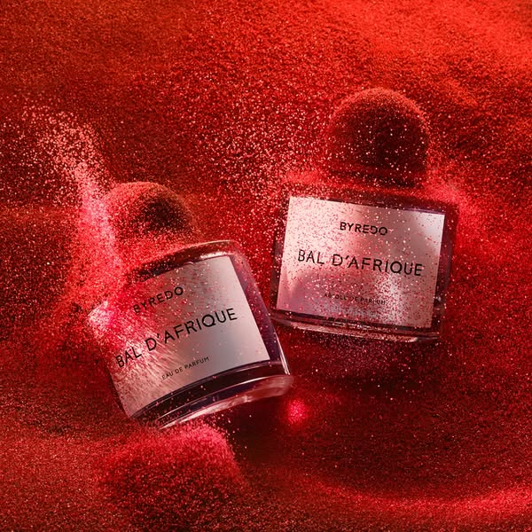 The ad features two bottles of Byredo's Bal d'Afrique Eau de Parfum on a red glittery surface. The ad focuses on