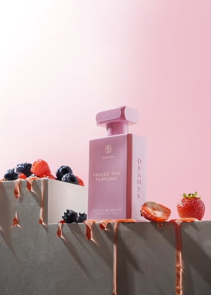 This ad showcases a bottle of OAKCHA perfume against a pink backdrop. The bottle is displayed alongside berries on a gre