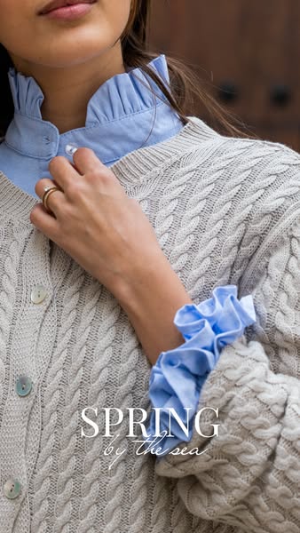 This image ad showcases a woman wearing a cozy cardigan over a ruffled blouse, promoting Spring by the Sea fashion brand