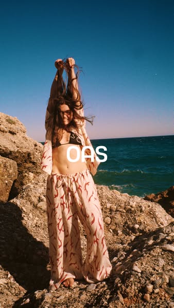 This image ad features a woman on a rocky outcrop by the ocean. She is wearing pants and a kimono-style top, both in the
