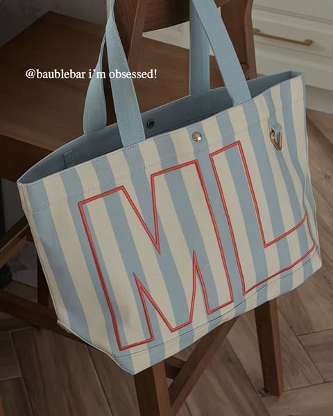This ad features a light blue and white striped BaubleBar tote bag with red block letters. The bag is being presented as