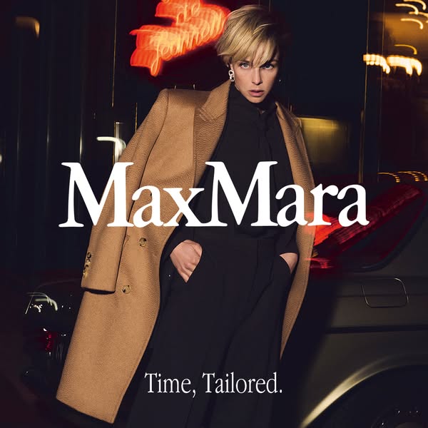 This MaxMara ad features a model in a camel coat and black ensemble against a blurred urban backdrop at night. The ad em