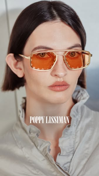 A close-up shot of a woman wearing Poppy Lissiman sunglasses with a gold frame and orange lenses. The brand name is prom