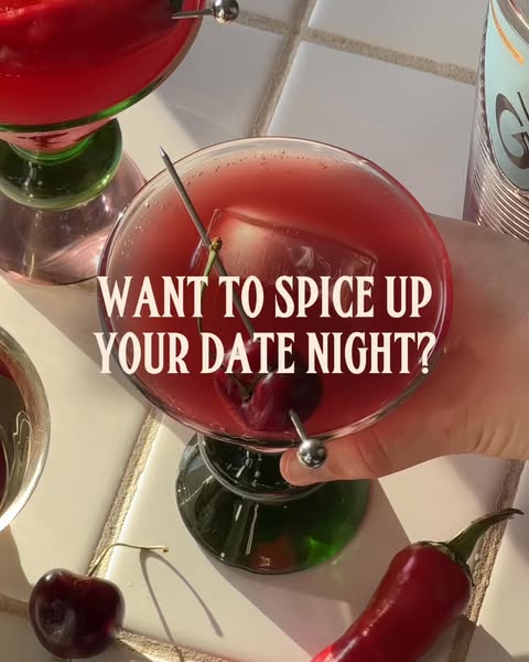 A close up shot of two cocktails, one in hand, on a tiled surface with a pepper and cherry, suggesting to the user that 