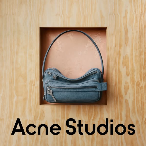 An ad for Acne Studios featuring a blue denim bag with a shoulder strap. The ad uses a simple product showcase format, w