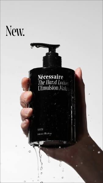 A minimalistic ad showcasing Nécessaire's The Hand Lotion. A hand is shown holding the bottle of hand lotion with wa