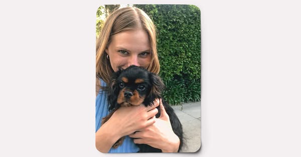 This is an image ad that features a smiling woman holding a dog in her arms in front of green foliage.
