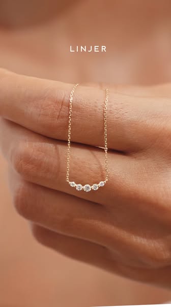 This ad displays a Linjer necklace being held up by a fair-skinned hand to showcase the product's design and feature