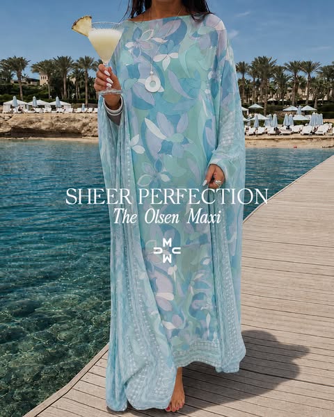 This image ad features a woman wearing a long, flowy maxi dress with a blue floral pattern. She is standing on a wooden 