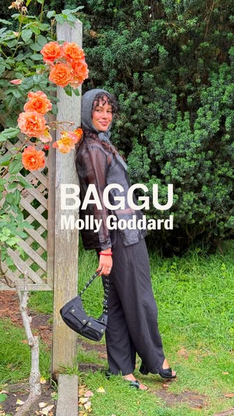 This image ad features a woman leaning against a wooden post with flowers, showcasing a black BAGGU purse. The ad highli