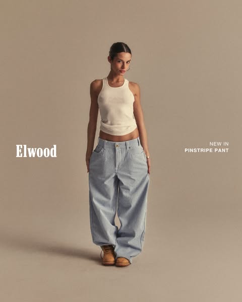 This Elwood ad features a full shot of a woman wearing their pinstripe pants and a white tank top.
