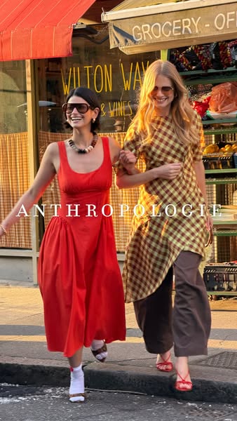This image ad promotes Anthropologie clothing featuring two women walking arm in arm in a casual outdoor setting with a 
