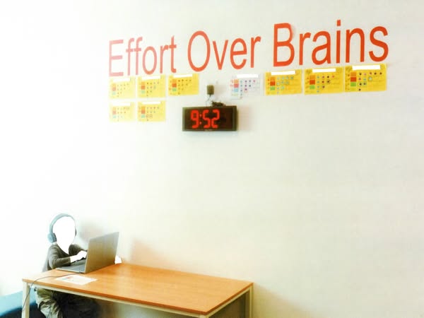 This ad features an image of a person working at a desk with the words "Effort Over Brains" written on the wal