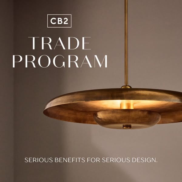 This ad promotes CB2's trade program. It features a close-up of a brass pendant light, set against a neutral wall, w