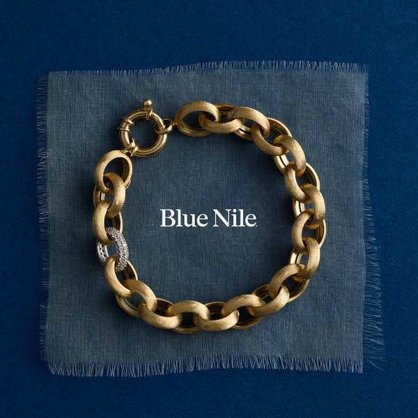 This image ad showcases a gold chainlink bracelet from Blue Nile. The bracelet is displayed on a piece of textured fabri