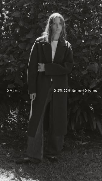 This black and white image showcases a woman modeling a long coat with the announcement of a sale.