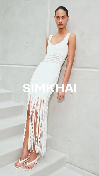 This ad features a woman in a white SIMKHAI dress, leaning against a wall near stairs. The neutral color palette, minima