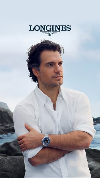 This ad features Henry Cavill wearing a Longines watch on a rocky coastline, set against a clear sky and ocean backgroun
