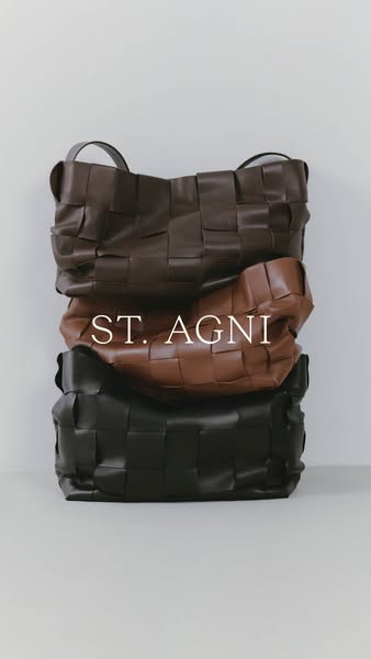 This image ad features a stack of three St. Agni woven leather tote bags in brown, tan, and black. The brand name is sup